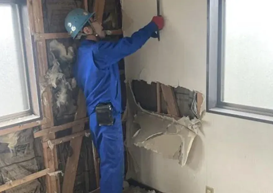 工具を手に持ち、解体作業を進める男性の写真。水色のヘルメットに青い作業服を着ている。